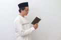 young Asian muslim man reading and reciting Holy book of Quran seriously. Isolated image on white background