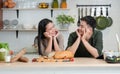 Portrait of young Asian romantic couple smiling, placing hands on chin, looking at each other in the kitchen Royalty Free Stock Photo