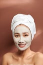 Portrait of young Asian wearing clay mask over brown background
