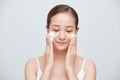 Portrait of young Asian woman applying foaming cleanser against white background