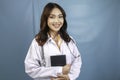 Portrait of a young Asian woman doctor, a medical professional is smiling and holding notes isolated over blue background Royalty Free Stock Photo