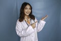 Portrait of a young Asian woman doctor, medical professional is smiling and pointing at a copy space isolated over blue background Royalty Free Stock Photo