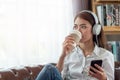 Young Asian woman enjoy listening to music with headphones and holding a hot cup of coffee, happy and relaxing time Royalty Free Stock Photo