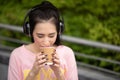 Young Asian woman enjoy listening to music with headphones and holding a hot cup of coffee, happy and relaxing time Royalty Free Stock Photo