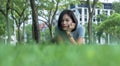 Portrait of young Asian woman enjoying and relaxing outdoors. Cheerful teenage female sitting on the green grass in the park on a Royalty Free Stock Photo