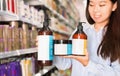 Portrait of young Asian woman holding kit of hair care products in supermarket Royalty Free Stock Photo