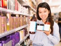 Portrait of young Asian woman holding kit of hair care products in supermarket Royalty Free Stock Photo