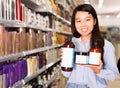 Portrait of young Asian woman holding kit of hair care products in supermarket Royalty Free Stock Photo