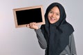 Portrait of young asian woman in islamic headscarf holding chalkboard. Smiling asian woman wearing islamic headscarf holding