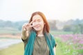 Portrait of young asian woman looking at camera with smile and showing peace sign with fingers with cosmos field in background Royalty Free Stock Photo