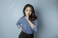 Portrait of a young Asian woman tell be quiet, shushing with serious face, hush with finger pressed to lips, isolated by blue Royalty Free Stock Photo