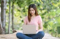 Portrait of young Asian woman using laptop outdoors. Smiling student girl sitting on bamboo table with computer, surfing the net Royalty Free Stock Photo