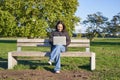 Portrait of young asian woman working on laptop, sitting on bench in park on sunny day, using her computer, studying in Royalty Free Stock Photo