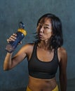 Portrait of young athletic and fit Asian Korean woman in fitness top holding drinking water bottle posing cool in bad girl defiant