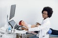 Portrait of young attractive african american female doctor, posing to camera with smile while conducting ultrasound