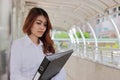 Portrait of young attractive Asian businesswoman holding document folder at pathway of outside office with copy space background. Royalty Free Stock Photo