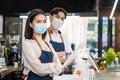 Portrait of young attractive Asian waiter and waitress wearing protective mask due to Covid-19 pandemic at cafe. Barista business Royalty Free Stock Photo