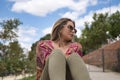 Portrait of a young, attractive and blonde woman, wearing cashmere shirt and green trousers, sitting on a stone wall, relaxed, on Royalty Free Stock Photo