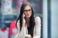 Portrait of young attractive business woman standing in the shopping mall with coffee and using her cell phone. Business break. Royalty Free Stock Photo