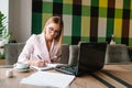 Portrait of young attractive businesswoman examining paperwork in bight light office interior sitting next to the window