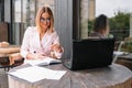 Portrait of young attractive businesswoman examining paperwork in bight light office interior sitting next to the window