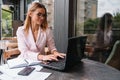 Portrait of young attractive businesswoman examining paperwork in bight light office interior sitting next to the window