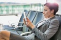 Portrait of young attractive businesswoman using digital tablet with earphones on while waiting for boarding in airport with lens Royalty Free Stock Photo