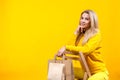 Portrait of young attractive caucasian blonde woman with paper eco bags in yellow sportive suit, sitting on a wooden chair, Royalty Free Stock Photo