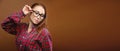 Portrait of a young attractive Caucasian woman in a red shirt and glasses on a brown background. Advertising glasses for Royalty Free Stock Photo