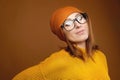 Portrait of a young attractive Caucasian woman in a yellow sweater and orange hat glasses on a brown background. Winter Royalty Free Stock Photo