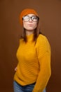 Portrait of a young attractive Caucasian woman in a yellow sweater and orange hat glasses on a brown background. Winter Royalty Free Stock Photo