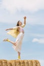 Portrait of young attractive dancing woman on top of haystack on blue sky background. Vertical frame