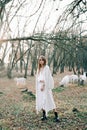 Portrait of a young attractive fair haired girl in a light white dress and black shoes in a picturesque forest with goats in Royalty Free Stock Photo