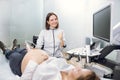 Portrait of young attractive female doctor, posing to camera with smile and thumb up, while conducting ultrasound