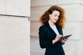 Portrait of young attractive female entrepreneur working on new business project using electronic gadget, having pleased look into Royalty Free Stock Photo