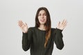 Portrait of young attractive female with long brown hair holding her arms in surrender gesture with loathing and