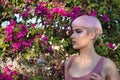 Portrait of young, attractive, gay, heavily makeup man with pink hair and top, staring into infinity with a bougainvillea