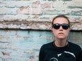 Portrait of young attractive girl in black t-shirt and sunglasses in rock style on urban background listening to music Royalty Free Stock Photo