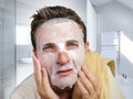 Portrait of young attractive and happy gay man in bathroom using beauty paper facial mask touching his face looking to the mirror Royalty Free Stock Photo