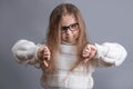 Portrait of a young attractive little girl with blond hair in sweater dissatisfied skeptic showing thumbs down dislike,disapproval Royalty Free Stock Photo