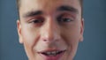 Portrait of a young attractive man malevolent talking directly to the camera on a gray background in studio. Close up