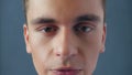 Portrait of a young attractive man malevolent talking directly to the camera on a gray background in studio. Close up