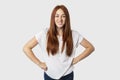 Portrait of young attractive redhead woman isolated on white background standing with her hands akimbo, frowning and showing teeth