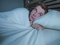 Portrait of young attractive scared man in fear and panic suffering horror nightmare covering face with blanket sleepless at night