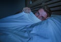 Portrait of young attractive scared man in fear and panic suffering horror nightmare covering face with blanket sleepless at night