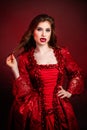 Portrait of a young, attractive vampire woman in a red rococo dress posing isolated against a dark background with red backlights Royalty Free Stock Photo