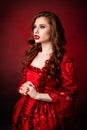 Portrait of a young, attractive vampire woman in a red rococo dress posing isolated against a dark background with red backlights Royalty Free Stock Photo