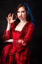 Portrait of a young, attractive vampire woman in a red rococo dress posing isolated against a dark background with blue backlights Royalty Free Stock Photo