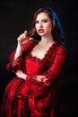 Portrait of a young, attractive vampire woman in a red rococo dress posing isolated against a dark background with blue backlights Royalty Free Stock Photo