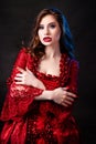 Portrait of a young, attractive vampire woman in a red rococo dress posing isolated against a dark background with blue backlights Royalty Free Stock Photo